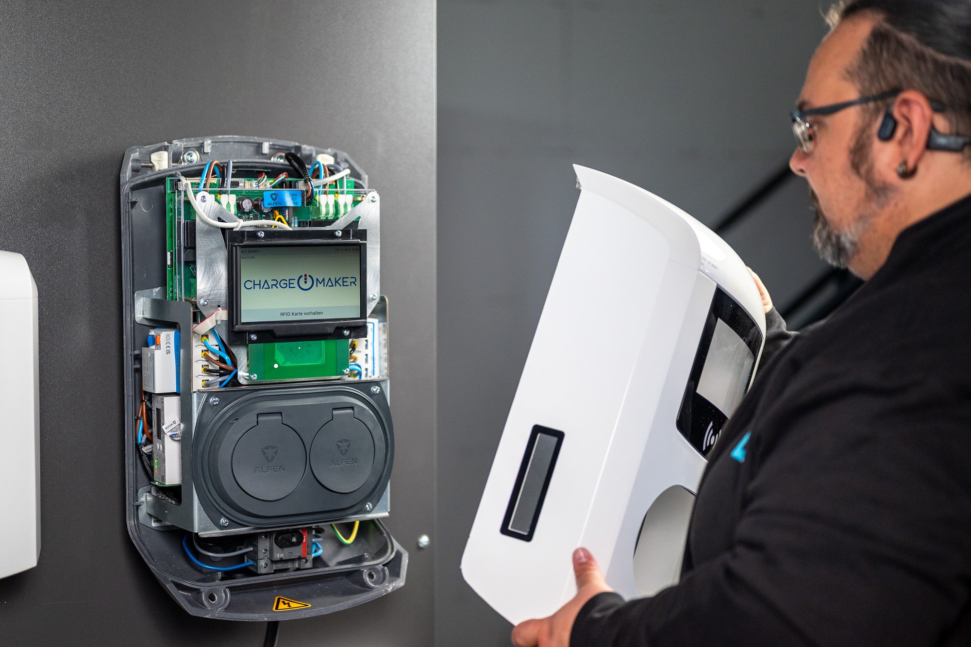 Ein Servicetechniker montiert die Gehäuseabdeckung einer offenen Wallbox vom Typ Charge Maker nach Installations- oder Wartungsarbeiten